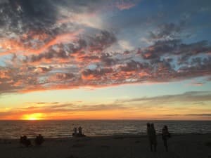 Sunset over the ocean with colorful clouds and silhouettes of people on the beach.