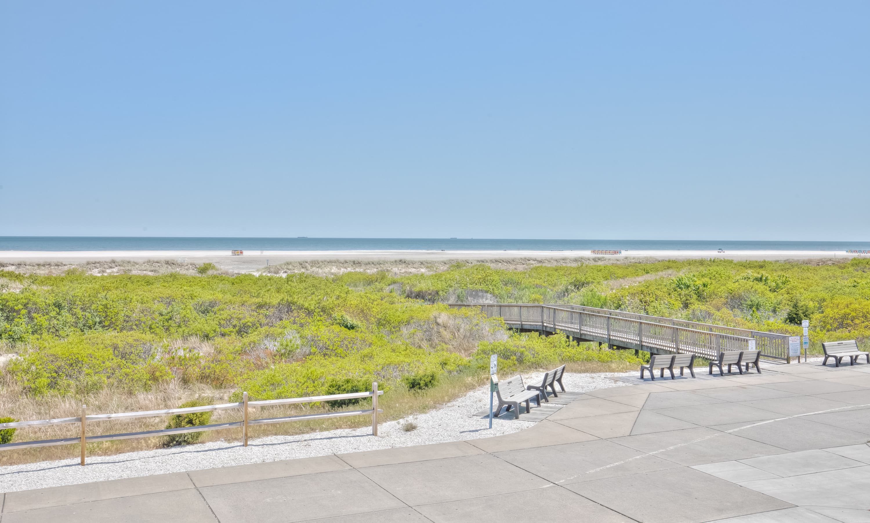 A sunny beach view with dunes, a boardwalk, and a clear blue sky.