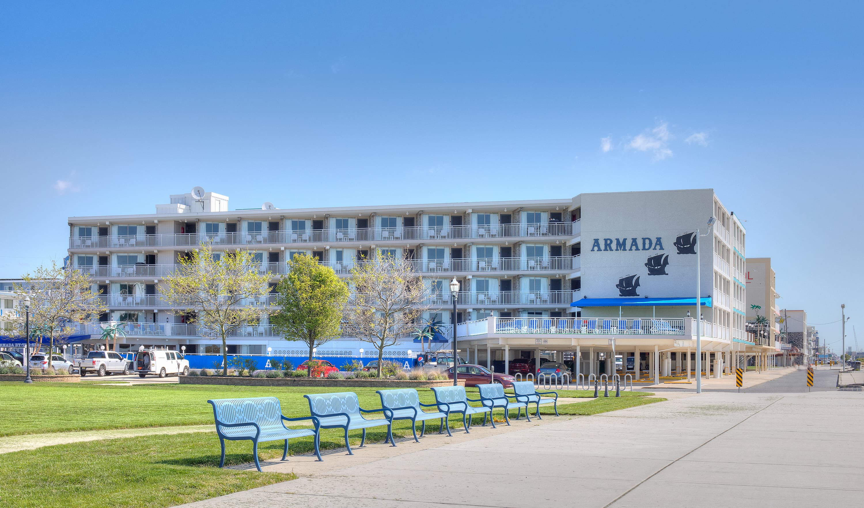 The Armada hotel stands prominently alongside a park with blue benches and green trees under a clear sky.