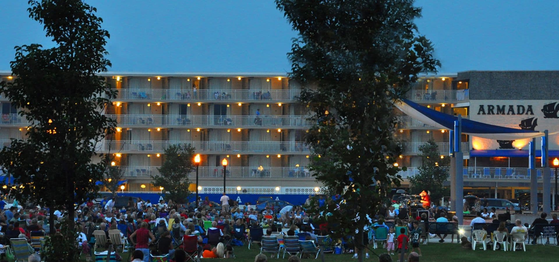 A crowd gathers in front of a lit motel with a sign reading "ARMADA" during dusk.