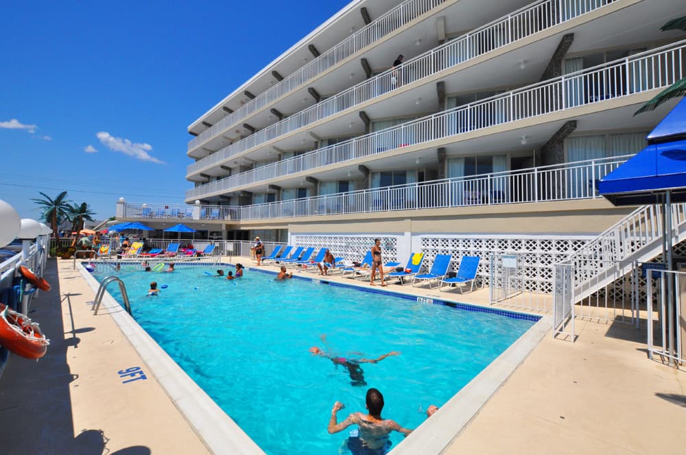 A sunny poolside scene with people swimming and lounging near a hotel.