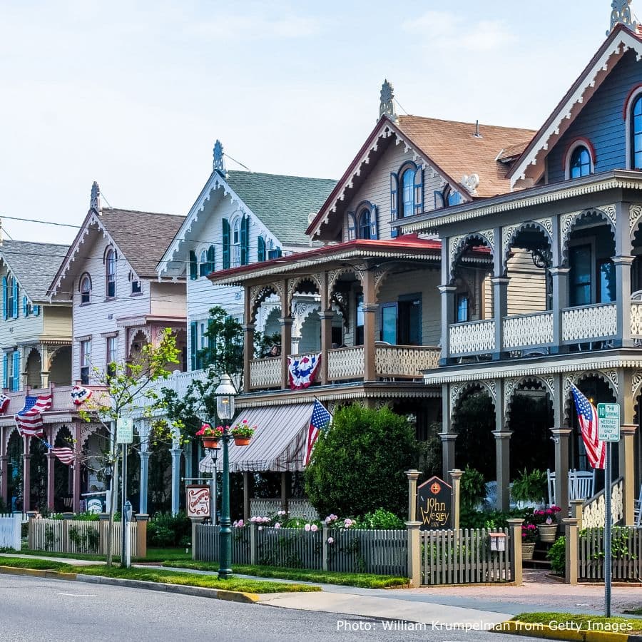 A row of Victorian-style houses with decorative porches and American flags lining the street.
