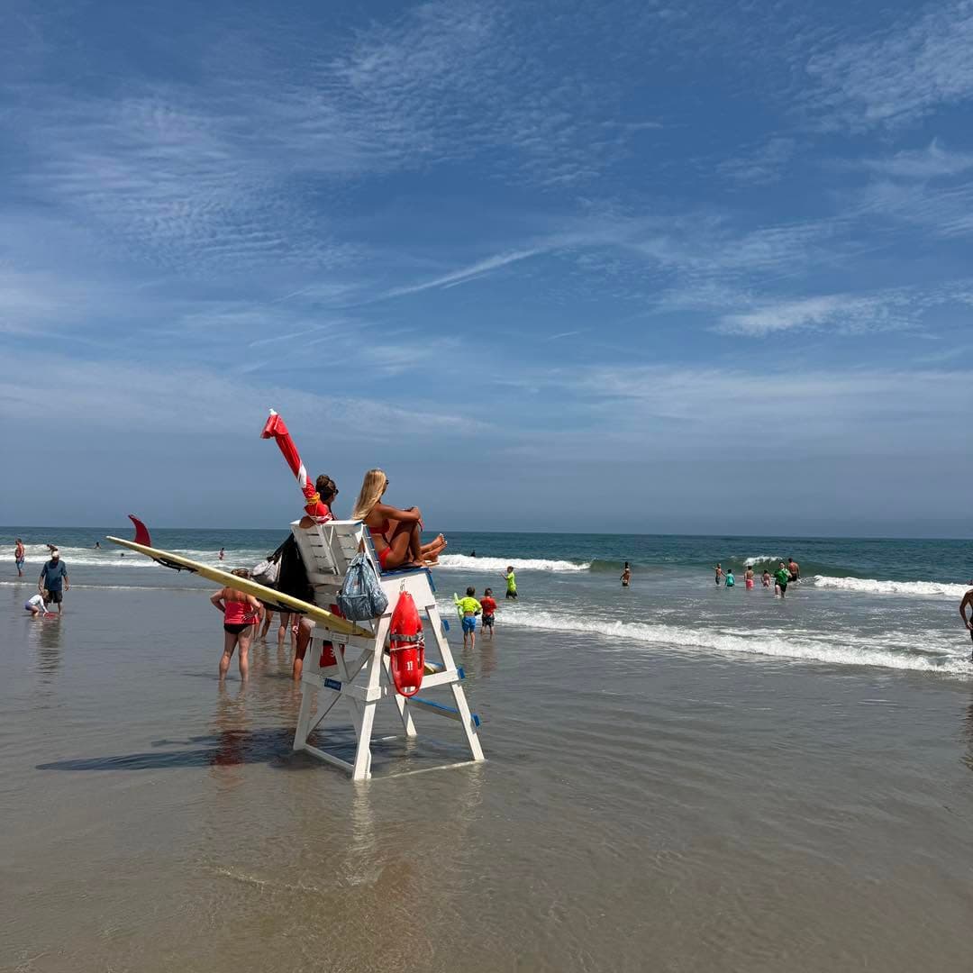 Lifeguards oversee beachgoers enjoying the ocean on a sunny day.