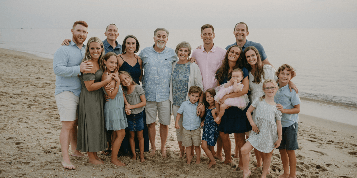 A large family gathers on the beach for a group photo at sunset.
