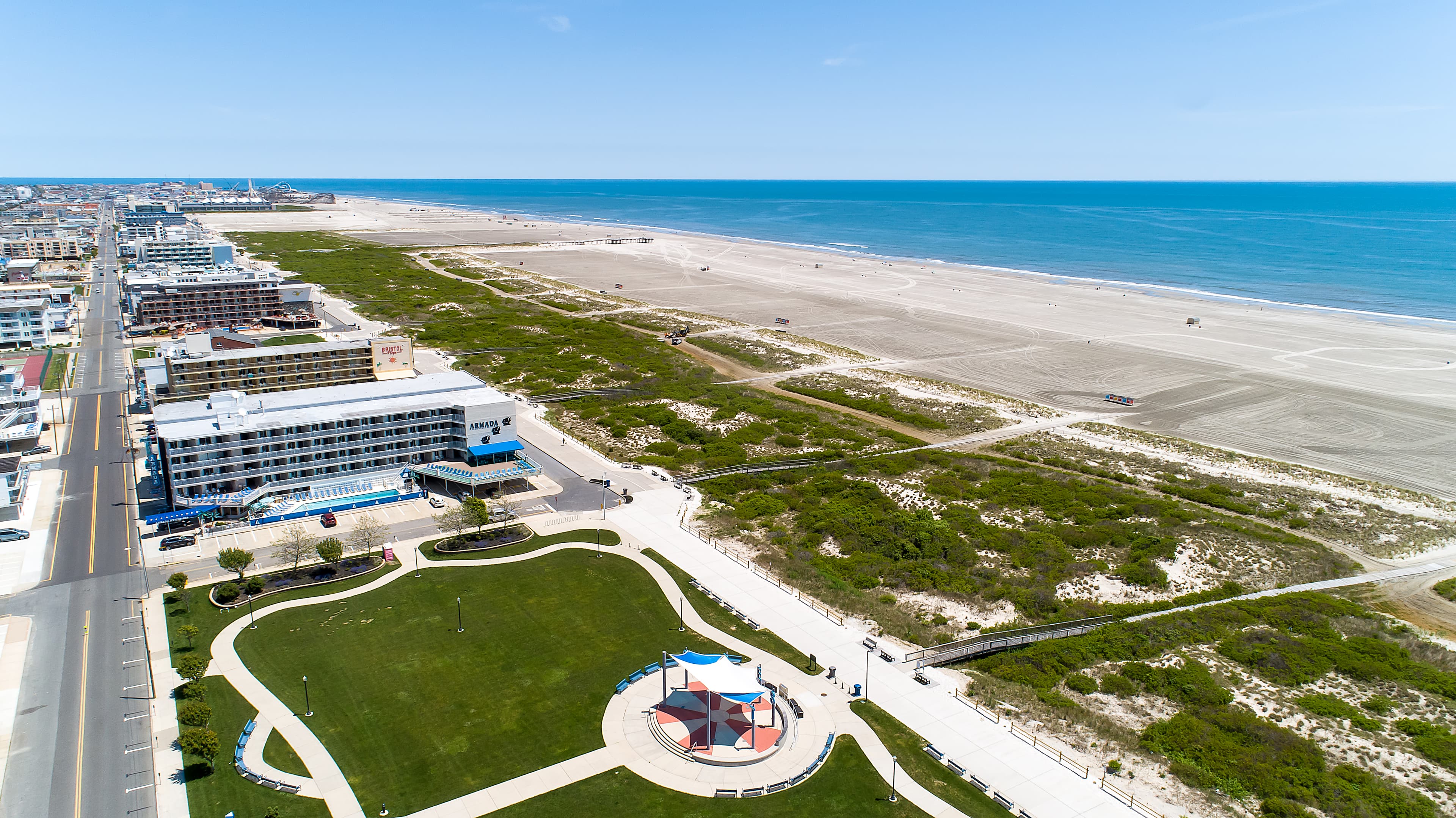 Aerial view of a coastal area featuring a beach, a green park, and nearby buildings.