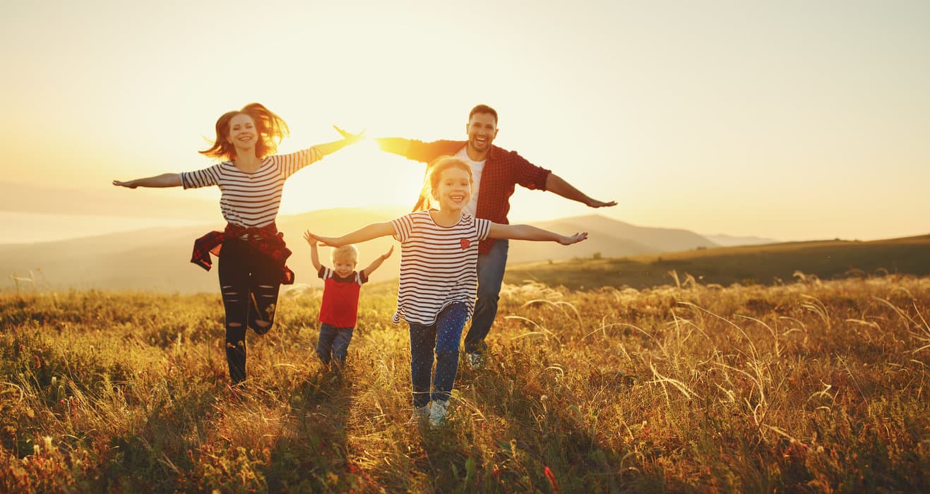 A joyful family runs together in a field at sunset.