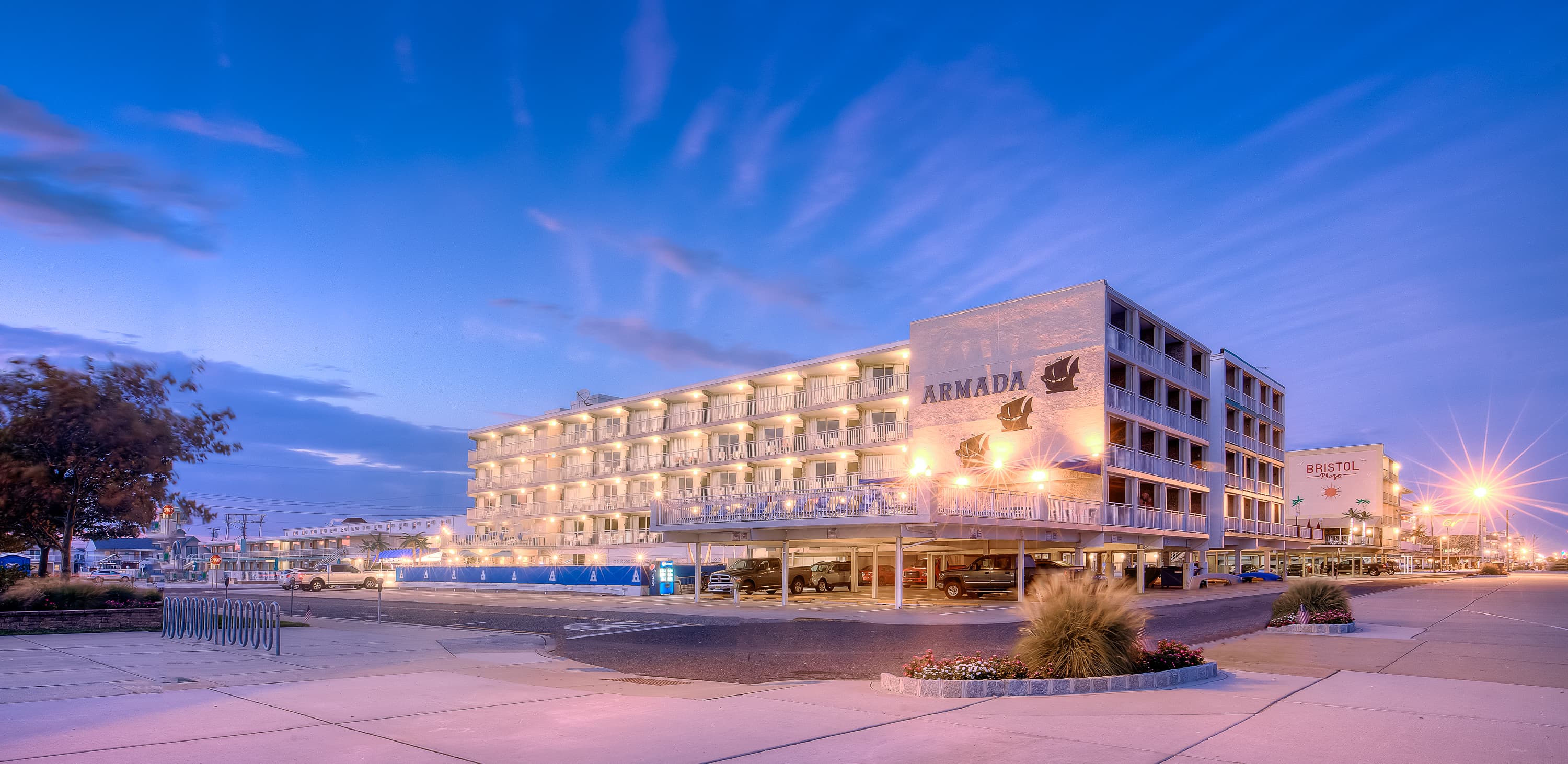 The Armada hotel building illuminated at dusk, with parked cars and palm landscaping in the foreground.