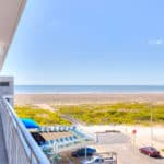 View from a balcony overlooking a sandy beach and ocean under a clear blue sky.