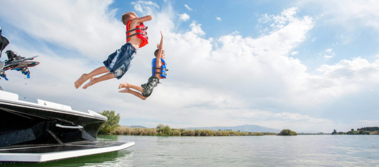 Kids jumping off the back of a boat into the water.