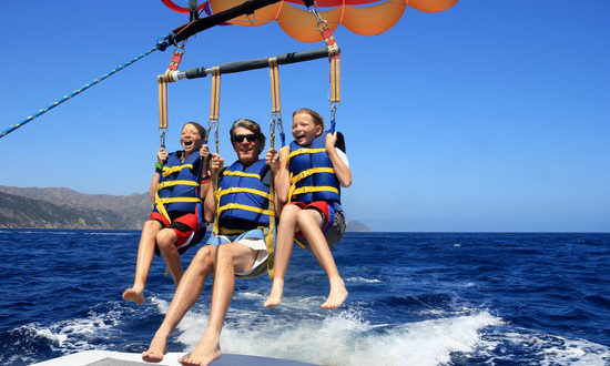 Father and Twin Daughters Parasailing Against a Blue Summer Sky.