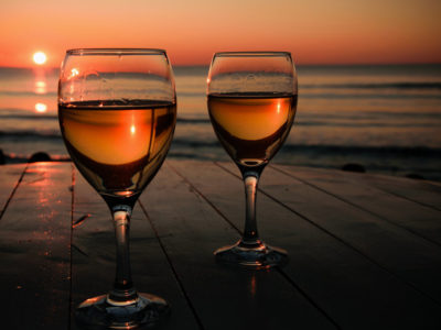 Romantic outdoor activity. Two glasses with white wine in an outdoor restaurant with sunset sea view, relaxation concept for two,